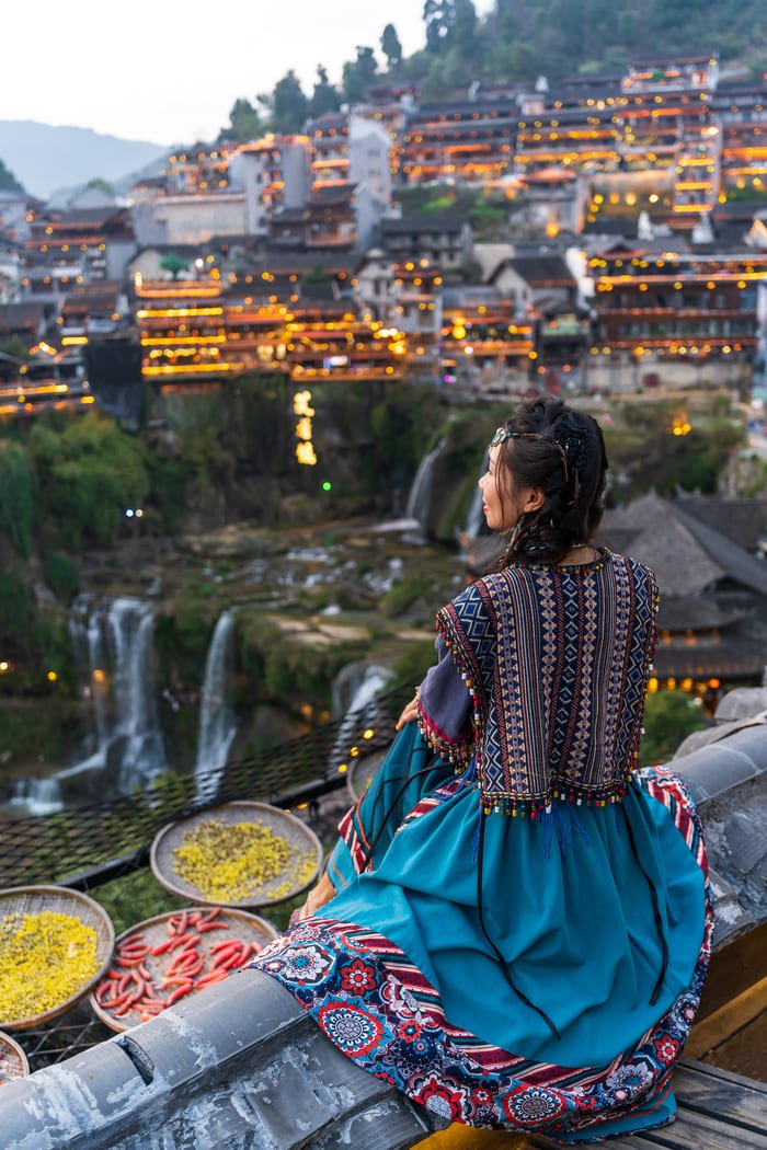 Una mujer china sentada y al fondo la ciudad de Lijiang